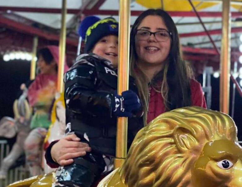 A woman rides a merry go round with a young boy. 