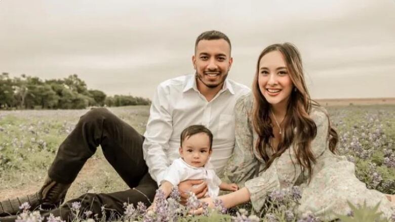 Two parents and a baby sit in a field of flowers.