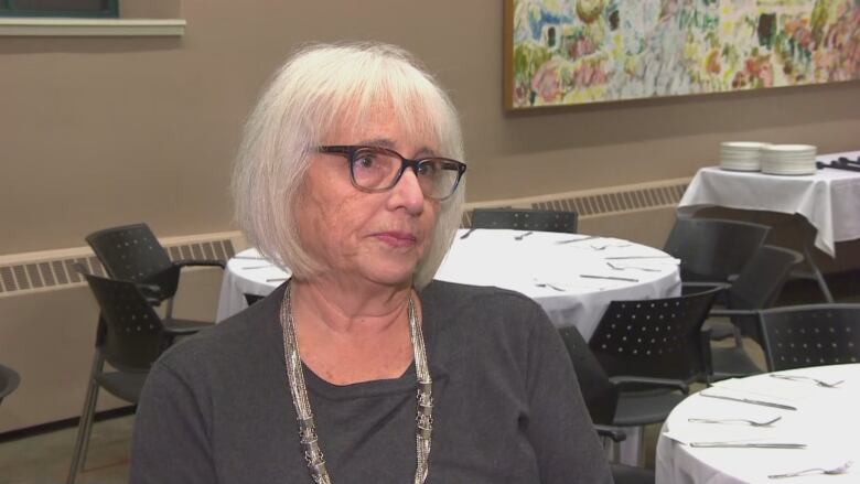 A woman with grey hair wearing a dark grey shirt.