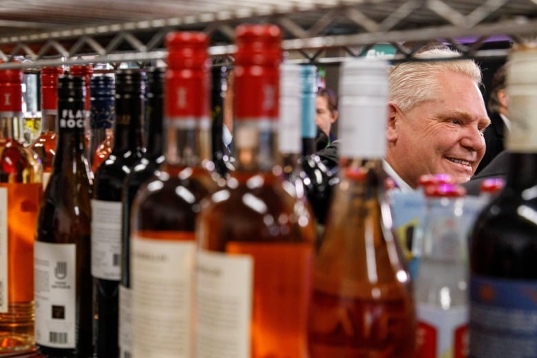 A white-haired man seen through racks carrying bottles of wine at a convenience store.