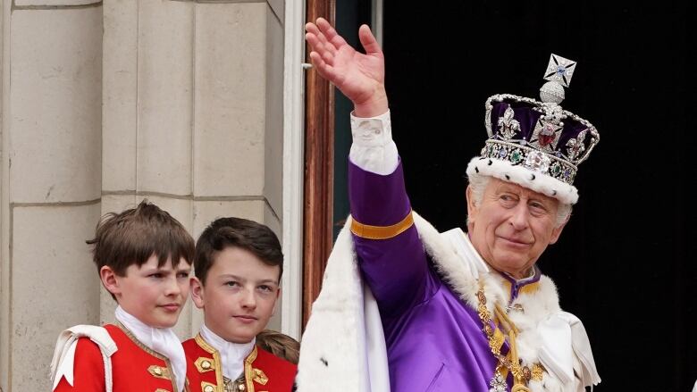 A person wearing a crown waves while two boys stand in the background.