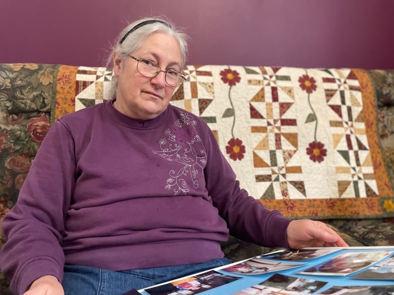 A woman in a purple sweater sits on a sofa and looks at a photo album.