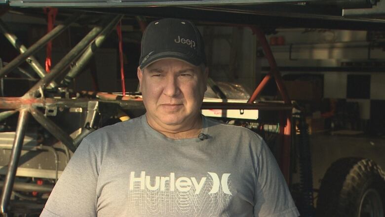 A white man in a baseball cap, standing in front of an autobody workshop inside his home