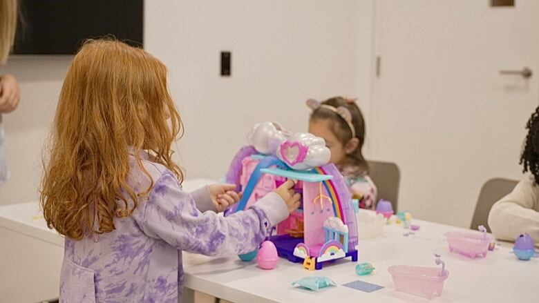 Three children are seen playing with toys at a white table in a white room. 