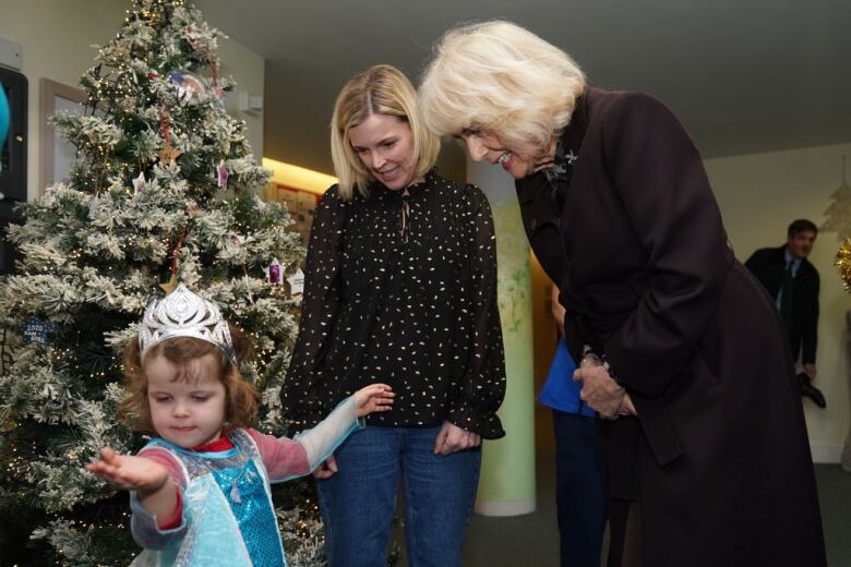 Adults look at a child as they all stand in front of a Christmas tree.