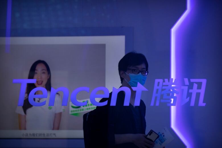 A visitor wearing a face mask walks past a logo for Chinese technology firm Tencent at their display at the China International Fair for Trade in Services (CIFTIS) in Beijing, Saturday, Sept. 5, 2020.