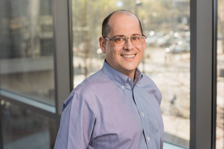 A smiling man in a pale blue shirt smiles for the camera.