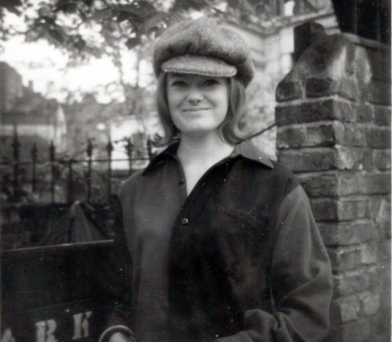 A black and white photo shows Susanna Blunt as a young woman. She is wearing a pageboy cap, a long-sleeved colour block button-up and has her hair in a shoulder-length bob.