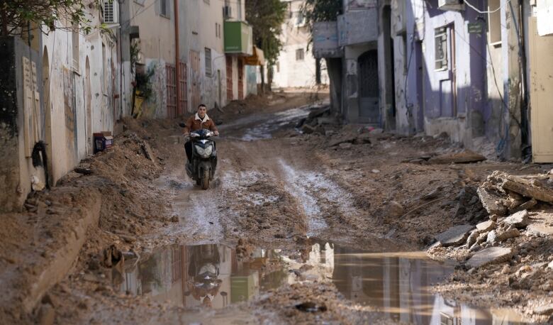 A man rides a motorcycle along a muddy street.