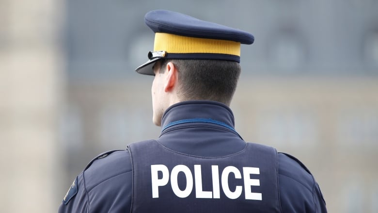 A police officer wearing a vest that reads, 'Police,' is photographed from behind.