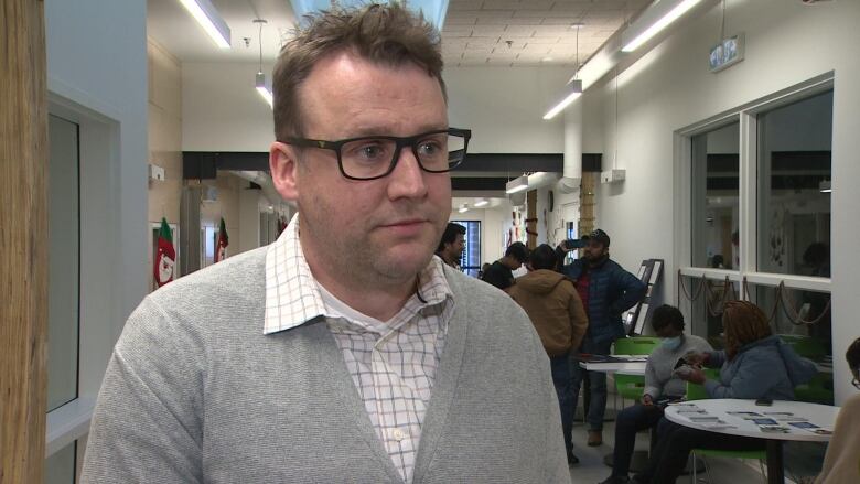 A man wearing glasses stands in a busy corridor.