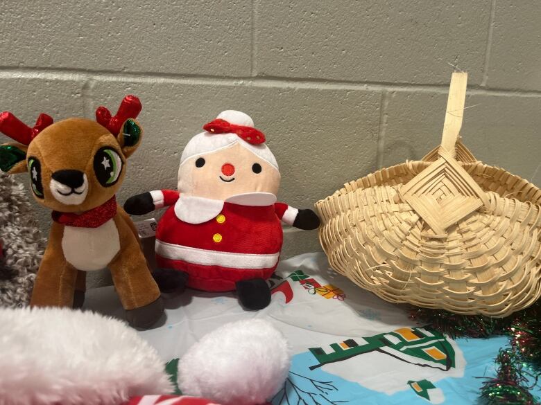 Two plushies of Santa and Rudolph sit on a table next to a woven basket. 