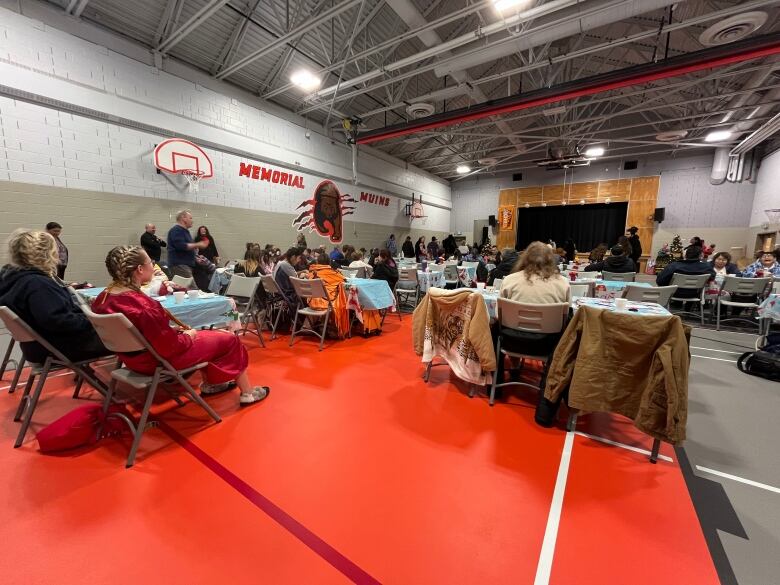 People sit in folder chairs facing the stage in a school gymnasium.