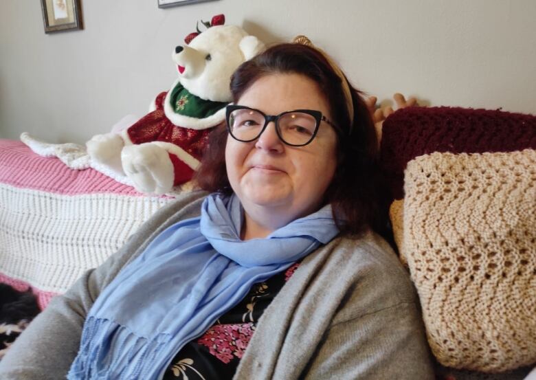 woman sitting on a couch, a teddy bear rests on the sofa behind her