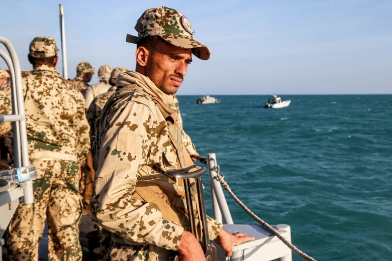 A man in camouflage gear on a boat looks out at the water.