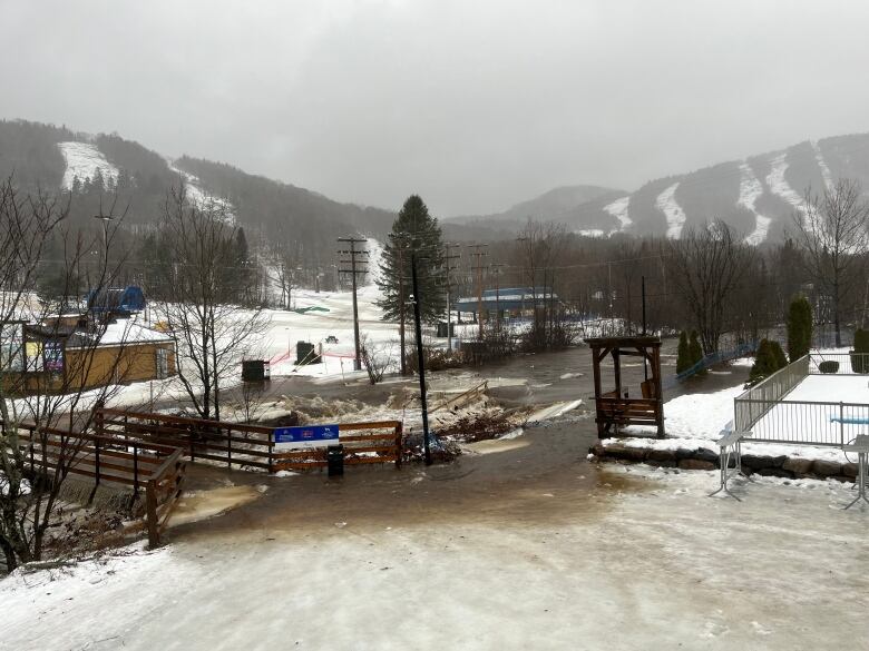 Gushing brown water in the foreground, ski trails in background.