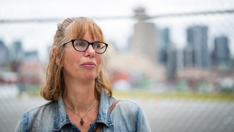 A white woman with reddish hair looks away from the camera, with a cityscape behind her in silhouette.