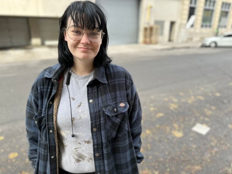 A woman stands on a street with a plaid shirt and dark hair.