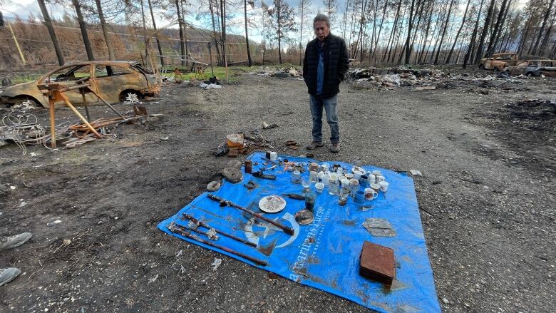 Man looks at recoverd burne objects on a blue tarp. 