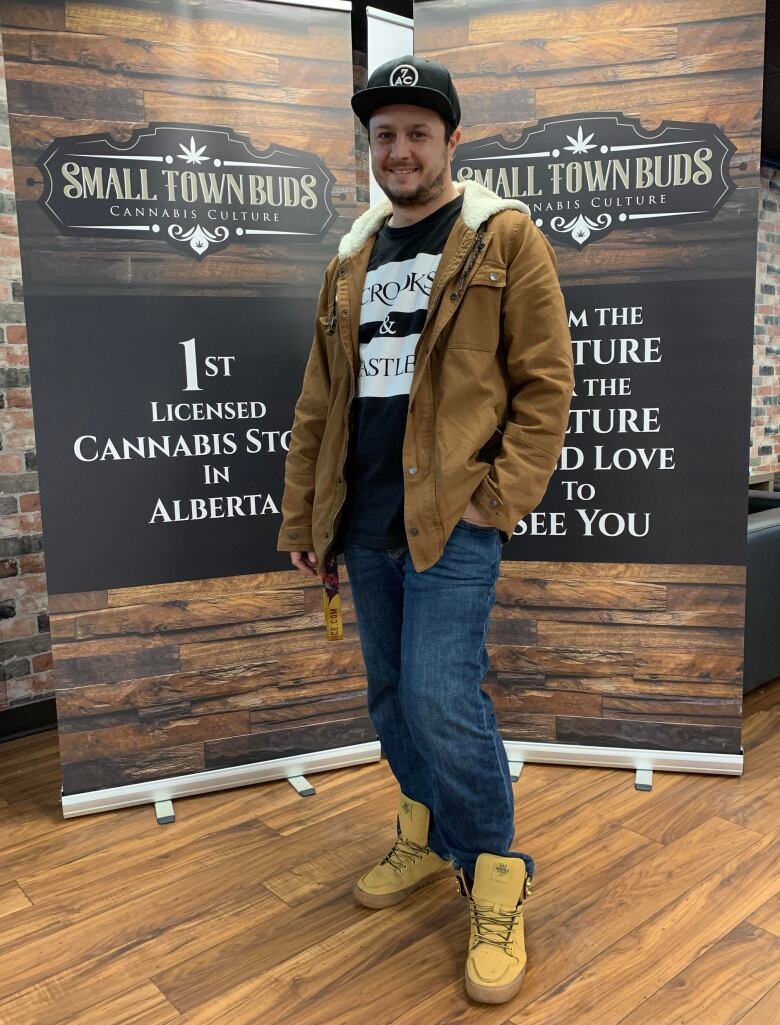 A man wearing jeans, a hoodie and a ball cap stands in front of a sign that says 