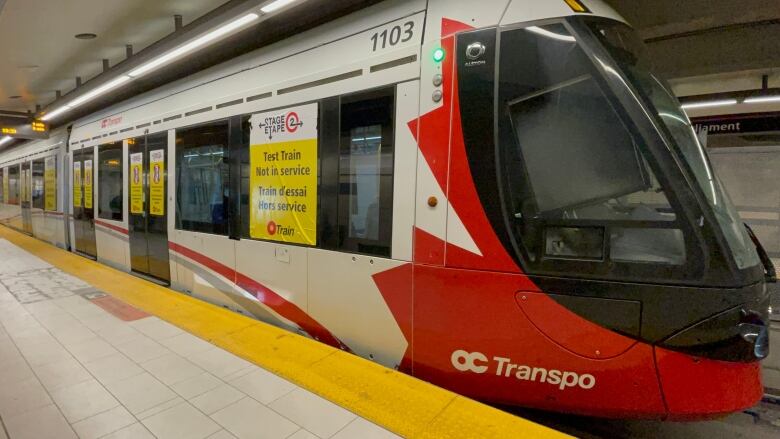 A red and white public transit train with big yellow stickers on it saying it's a test run.