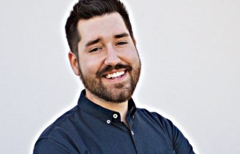 a man with dark hair and a button down shirt crosses his arms and smiles