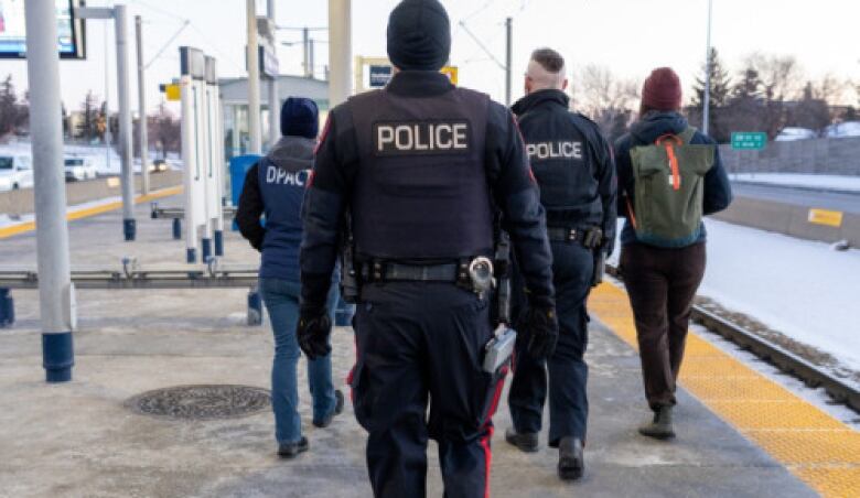 Two police officers and two outreach workers walk away from the camera on a CTrain station platform.