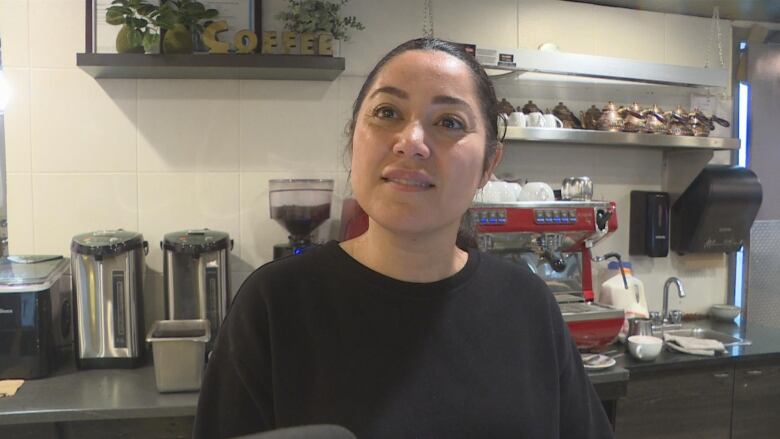 A woman speaks to a camera while at a cafe counter.