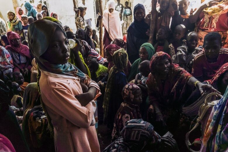 Dozens of people are shown sitting or standing in close proximity, many wearing robes and head coverings.