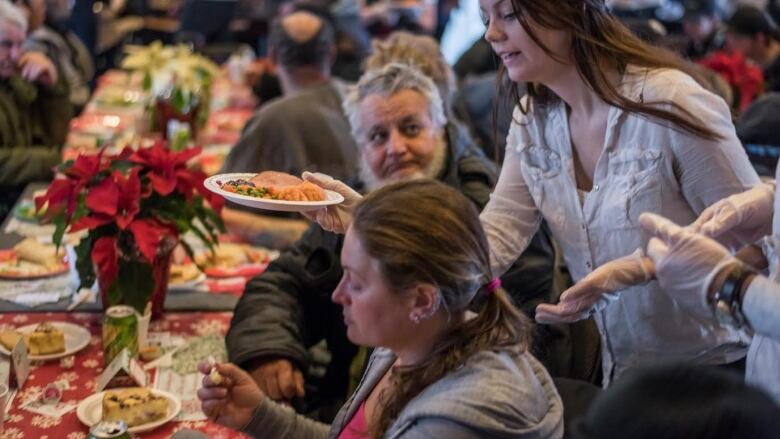 A women passing a plate of food to people 