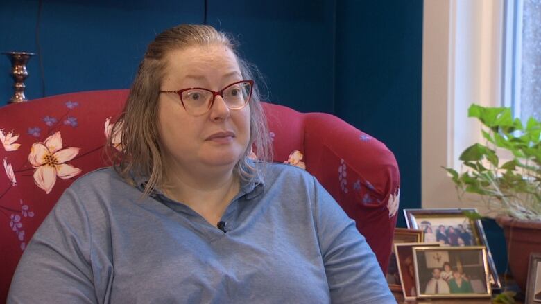 A woman in a blue shirt sits in an armchair. 