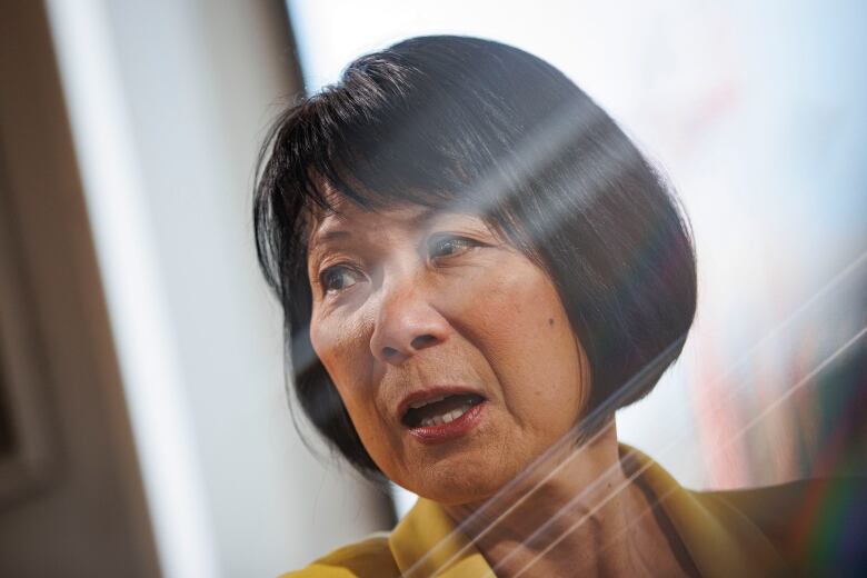 A woman is seen with shards of light shining over her face through a window.