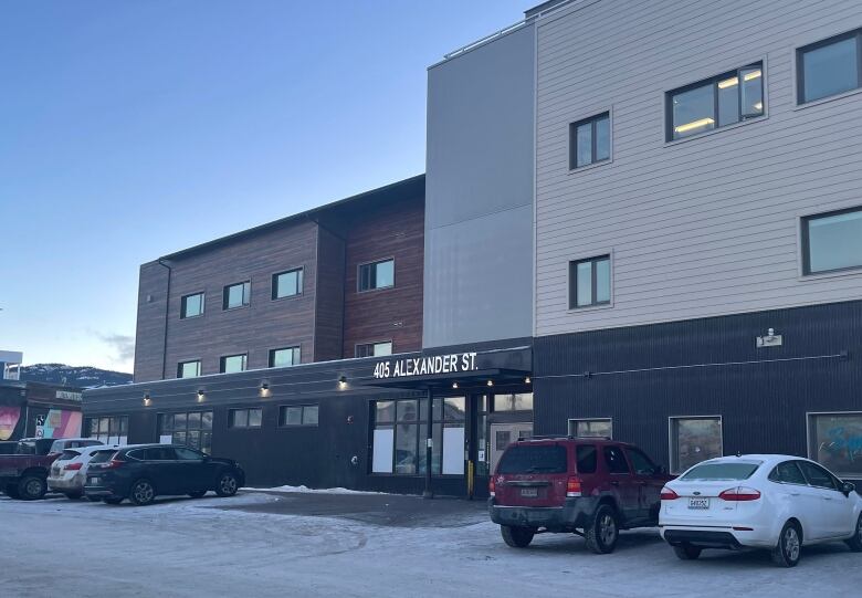 Cars are seen parked in front of a building  in winter. 