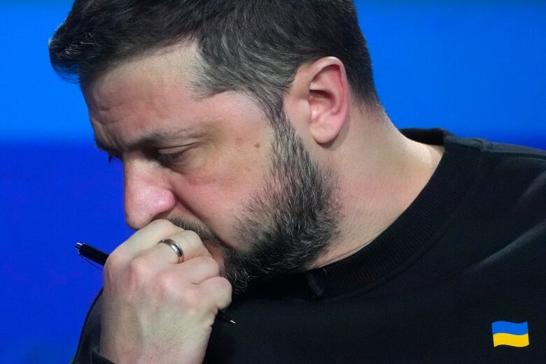 A pensive-looking bearded man looks away from the camera.