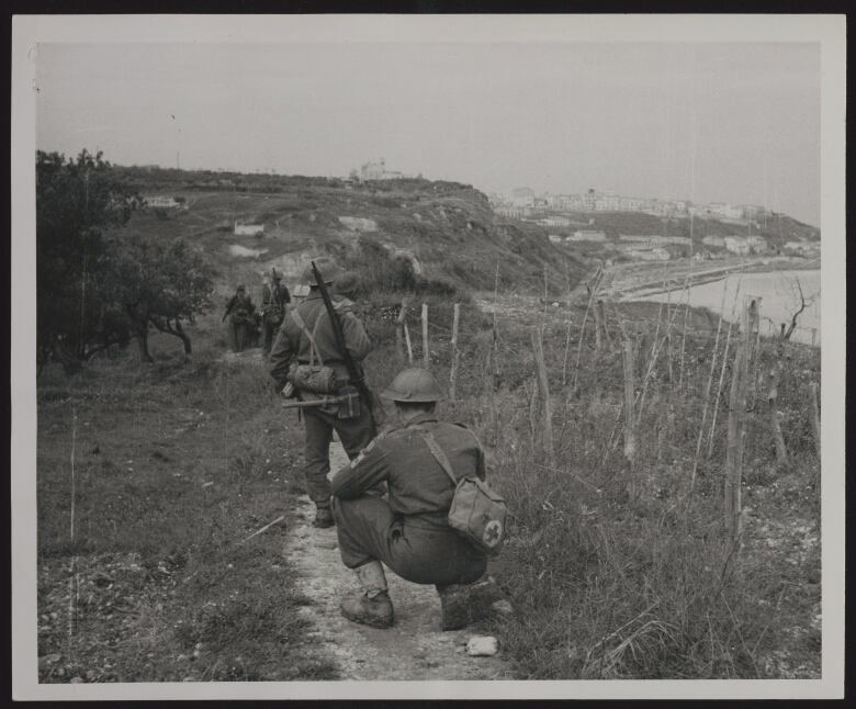 Canadian soldiers are shown walking through a narrow path along the Adriatic coast as they advance toward Ortona, Italy, in the Second World War.