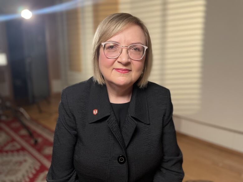 A woman in business attire looks into the camera.