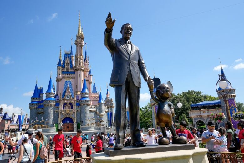 Close up of a large statue of Walt Disney and Mickey Mouse with the Magic Kingdom castle in the background, in the daytime at Disney World.