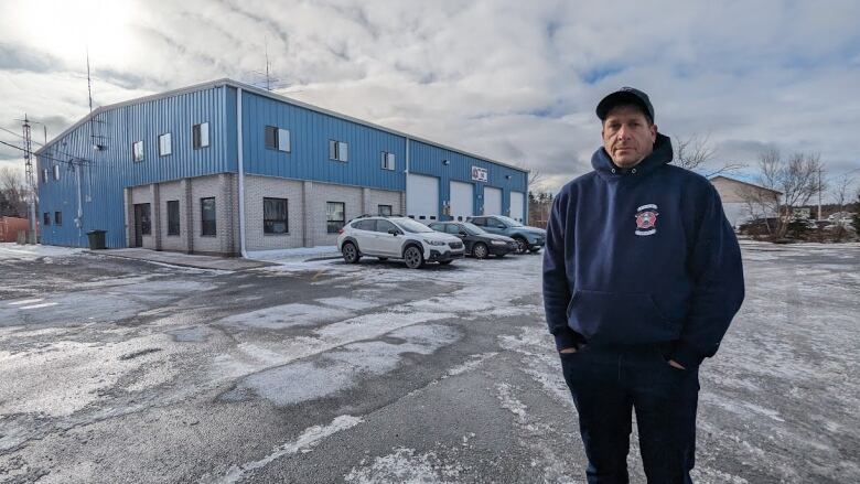 A man stands outside a blue building wearing a hoodie.