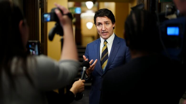 A man in a blue suit speaks in front of a bank of TV cameras.