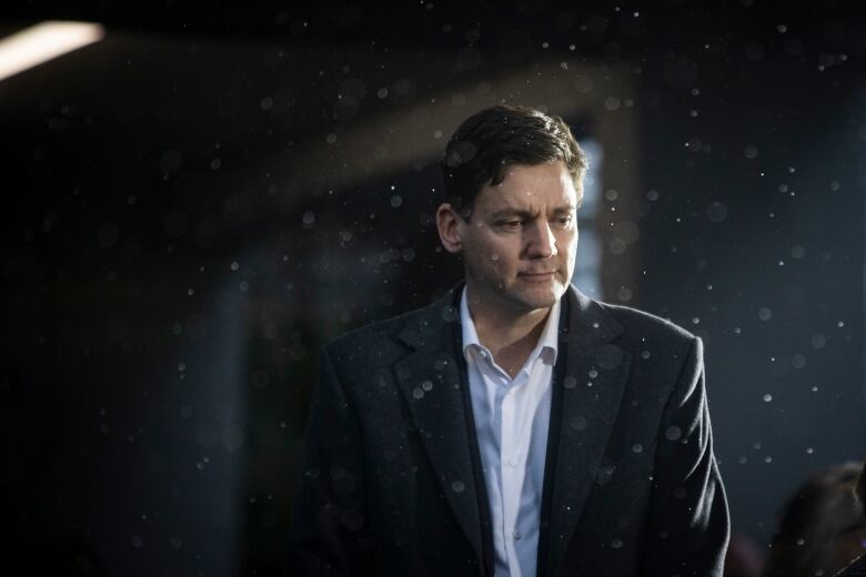 Premier David Eby in a suit with lights flashing in his face and specks of dust floating around during a press conference. 