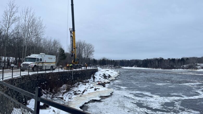 A crane near a river with some emergency officials nearby. 