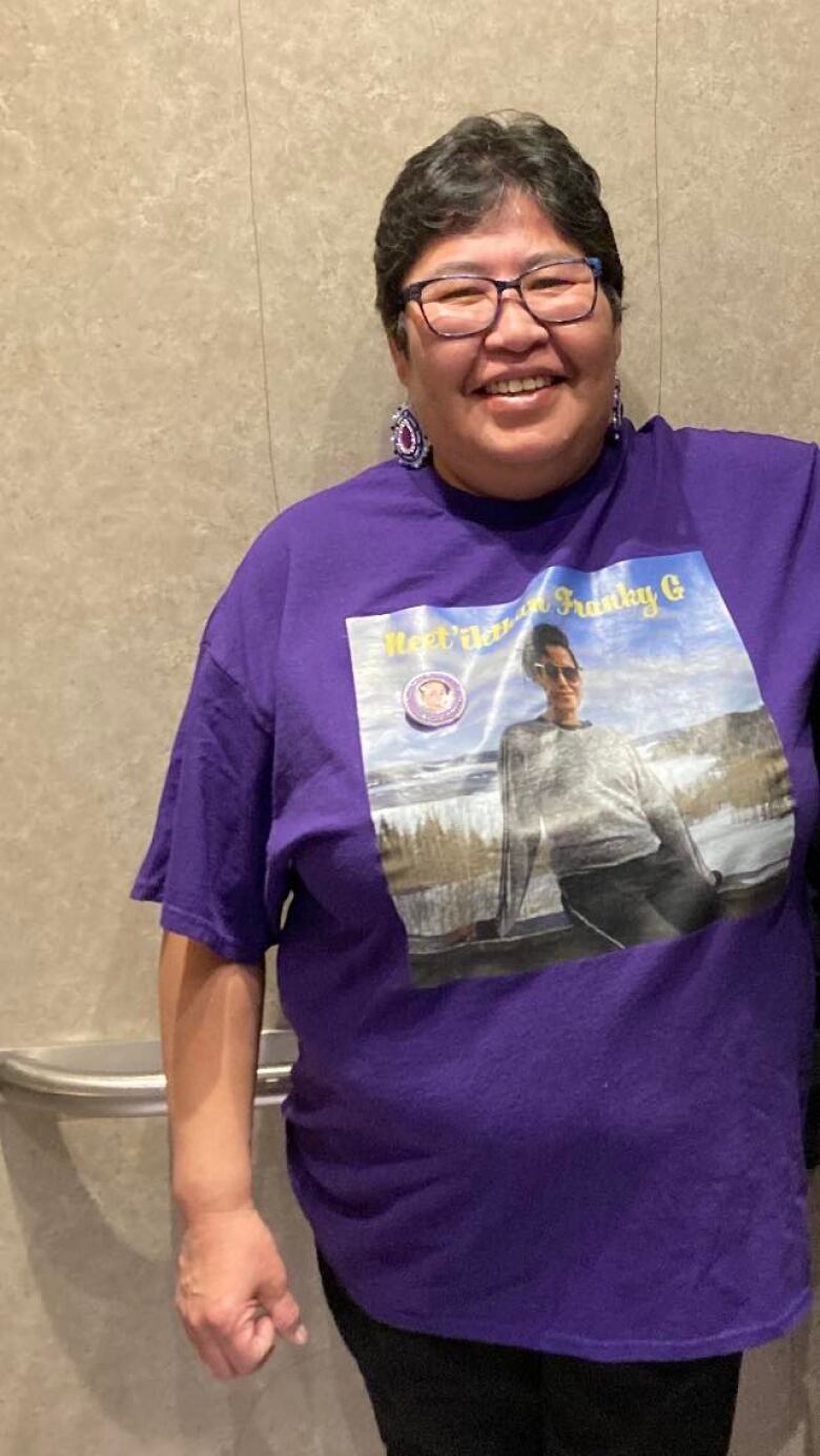 Woman smiling and wearing purple t-shirt with the face of her missing son on it