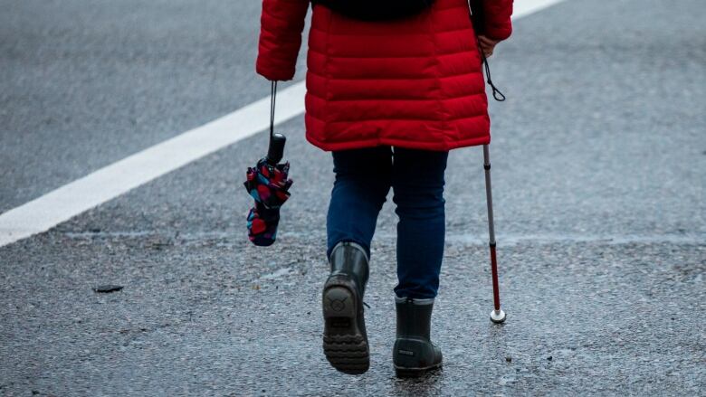 Someone walks down a street using a blind cane. 