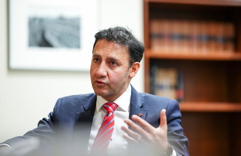 A man in a suit sitting in front of a bookshelf.