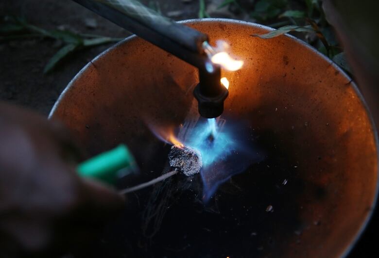 A closeup image shows a torch with a blue flame hovering over a ball of white metal in a pan. 