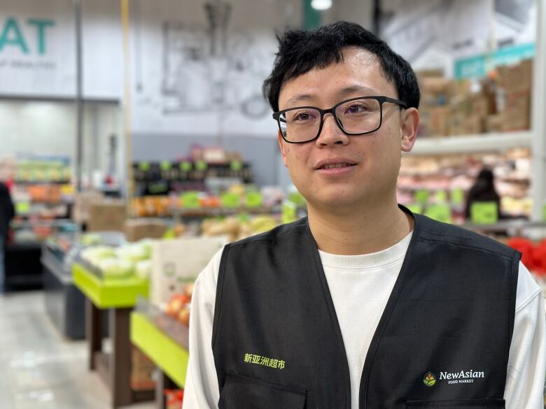 A man is shown wearing a black vest among fruits and vegetables in an Asian grocery store in Halifax.