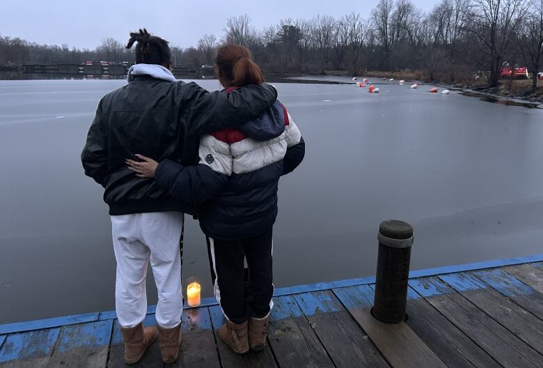 Two people look out into the river with a lit candle by their feet.