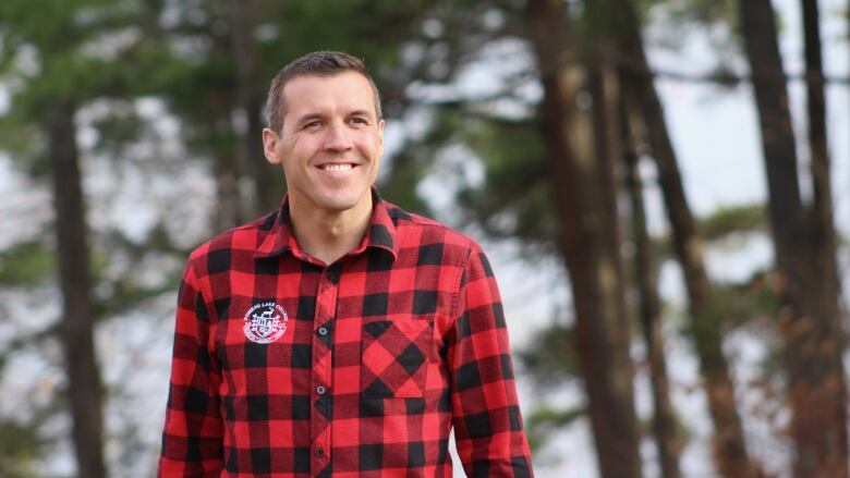 A man in a red and black plaid shirt smiles.