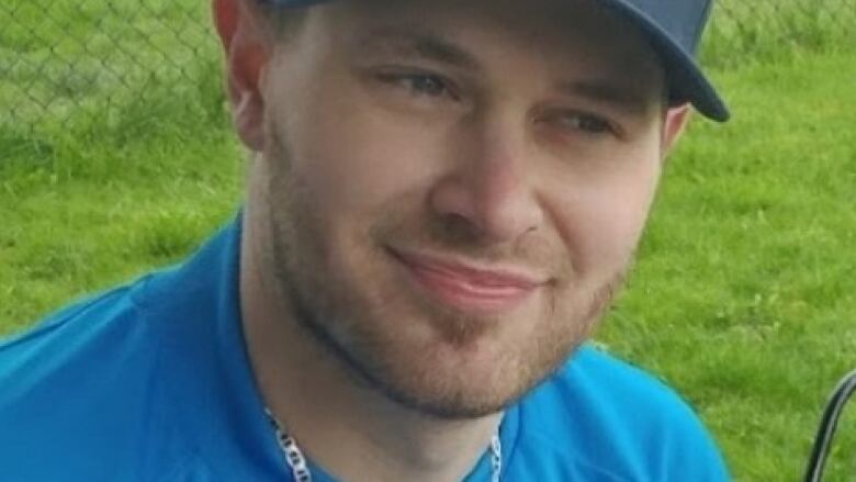 A young man with a baseball cap smiles slightly and looks away from the camera.