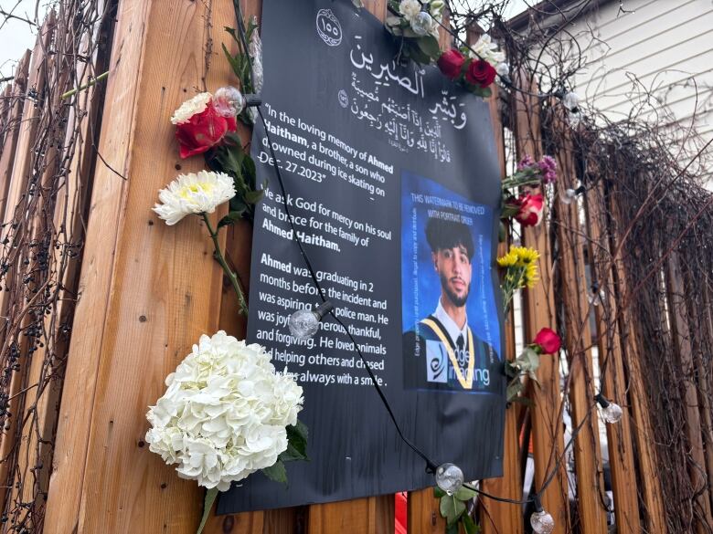 A portrait of a teen attached to a fence with flowers around it.